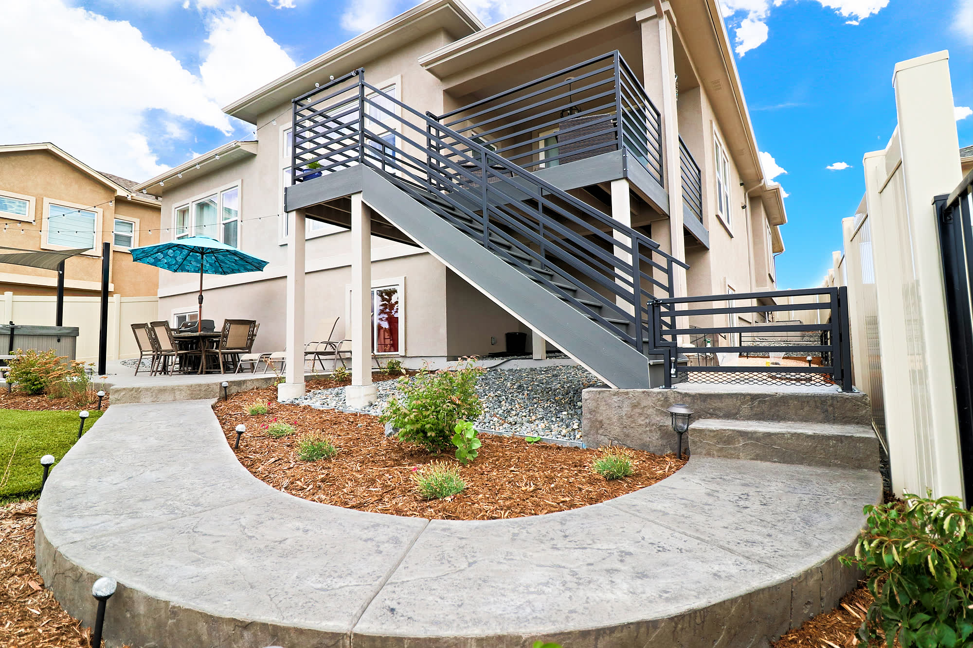 A composite deck with horizontal matte-black steel railing above a stamped-concrete patio at the Smith residence